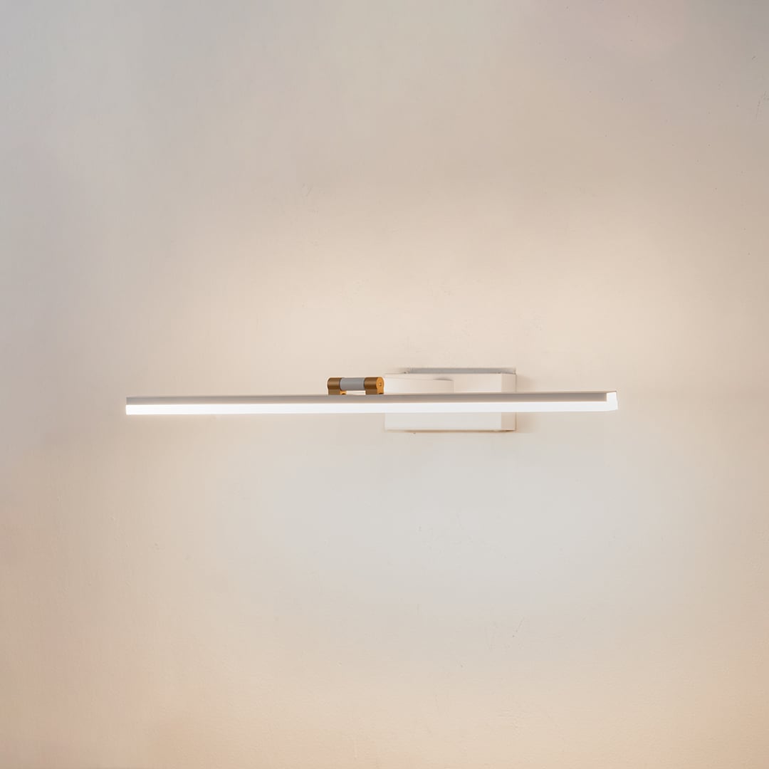 White and gold metal picture light glowing softly on a clean white background offering a sleek modern wall lighting look.