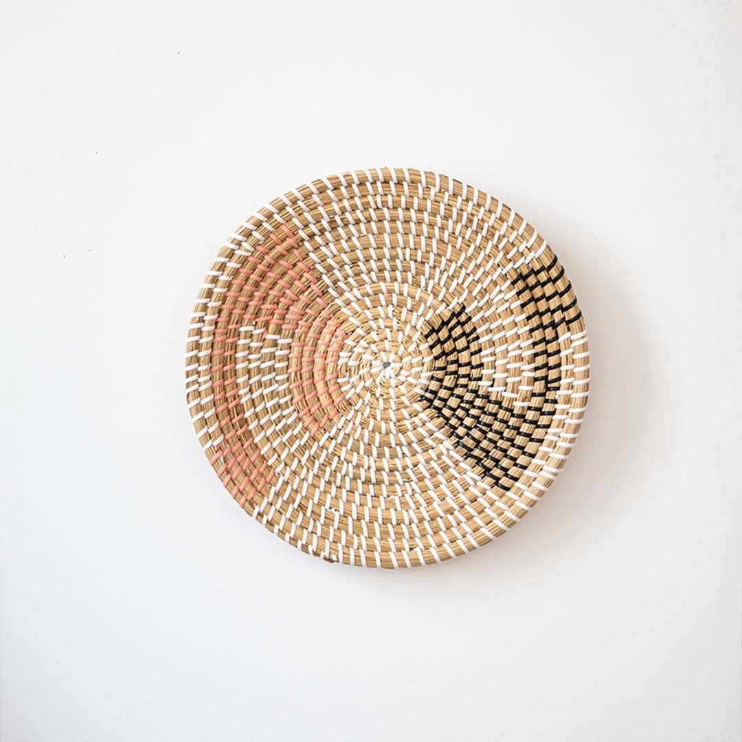 Handwoven wall basket in natural pink and black fiber with abstract design shown on white background