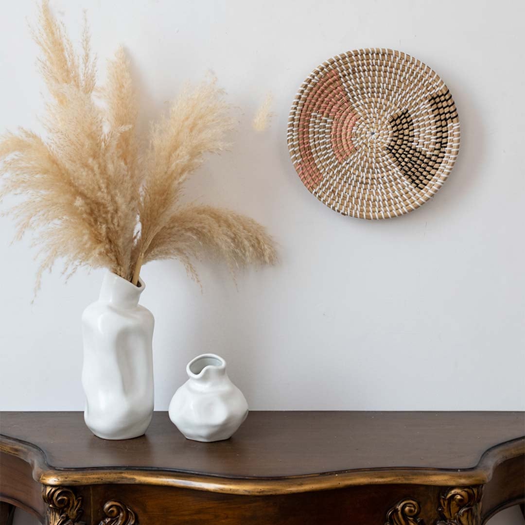 Handwoven wall basket decor in natural pink and black fiber styled above wooden console table for boho wall.