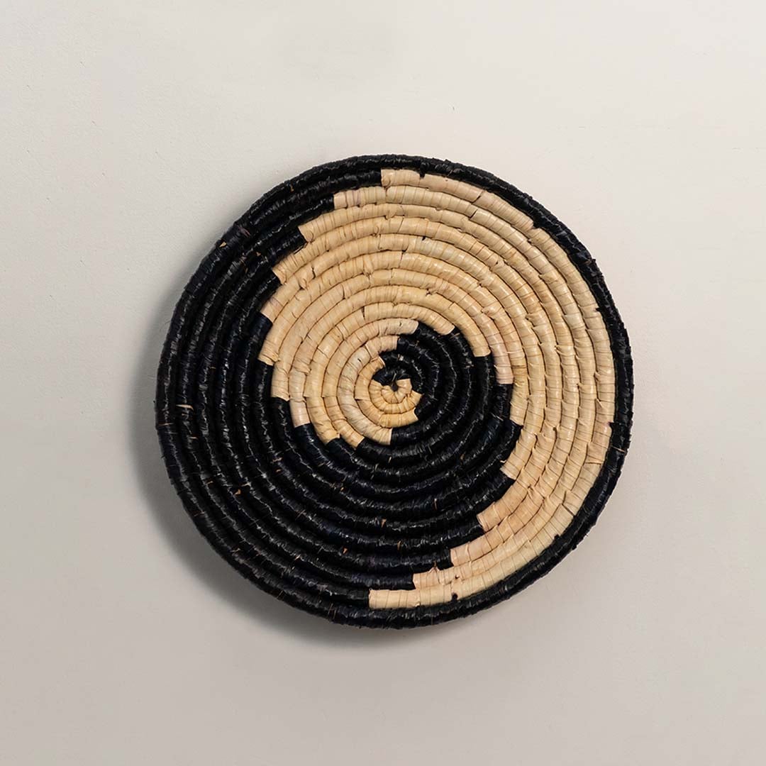A handwoven natural and black rattan decor plate displayed on a white background highlighting its spiral weaving and textured artisan design for modern wall decor.