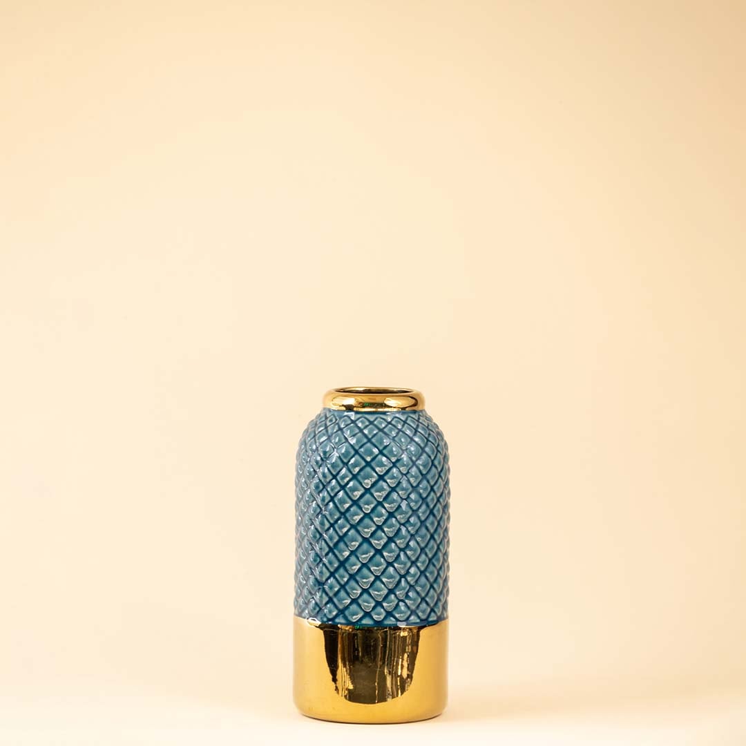 Blue textured vase with gold detailing and bright flowers displayed clearly against a minimalist white background.