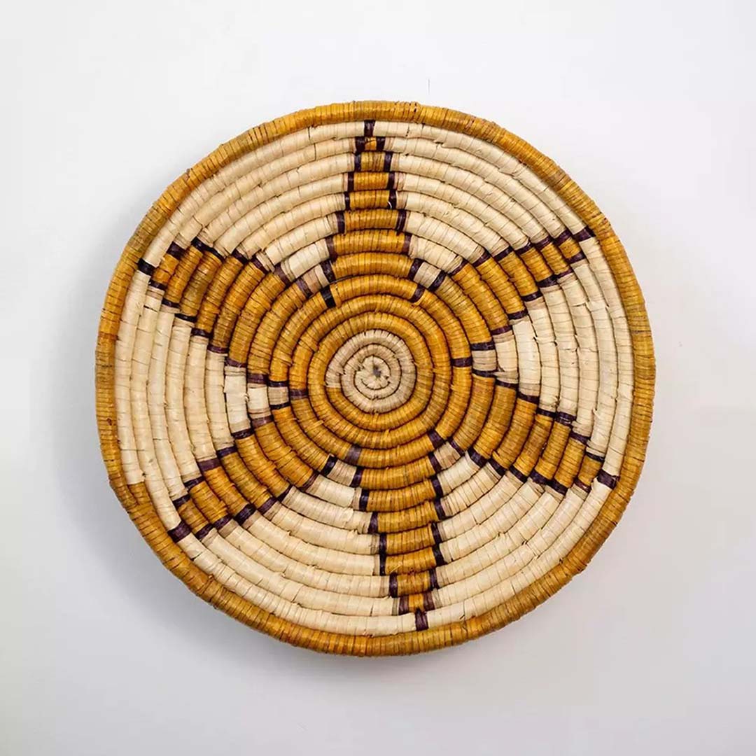 Round woven basket wall decor on white background with starburst design in beige and brown handmade natural materials.