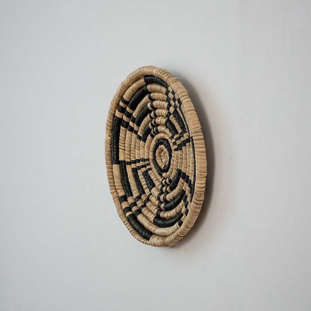 Side profile of round woven wall basket in seagrass with beige and black texture highlighting depth and handmade detail.