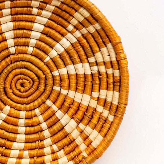 Closeup of detailed weaving texture and tribal-inspired pattern on mustard and white round wall basket.