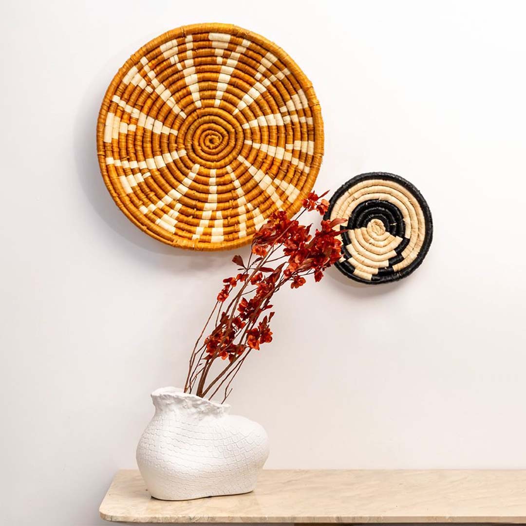 Large woven basket wall decor styled above wooden console with candle books and indoor plants.