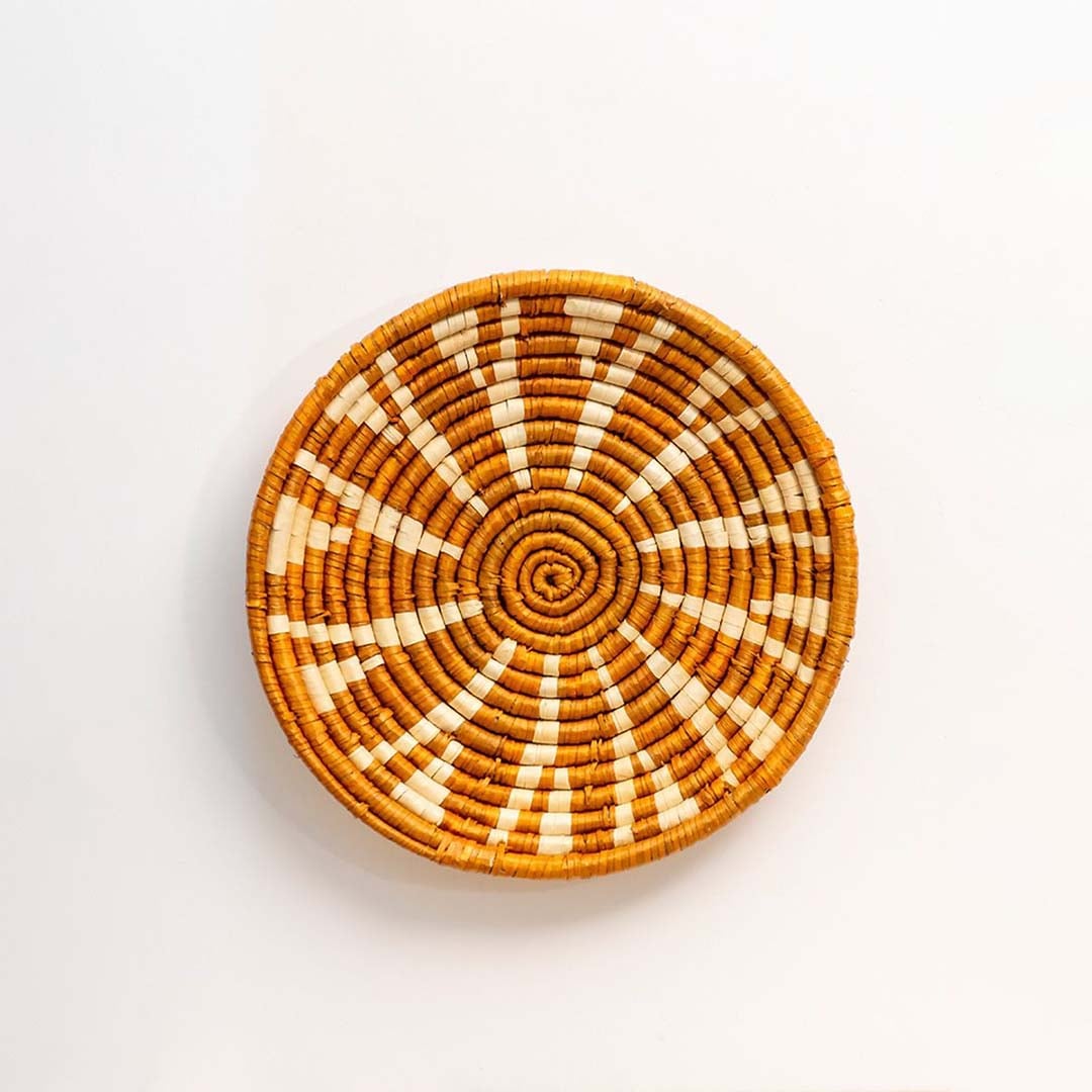 Round woven basket wall decor with mustard and white tribal pattern on plain white background.