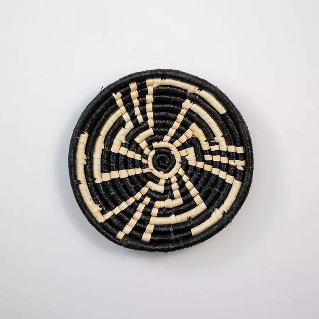 Decorative woven basket with striking black and beige geometric design on a plain white background ideal for wall art styling.