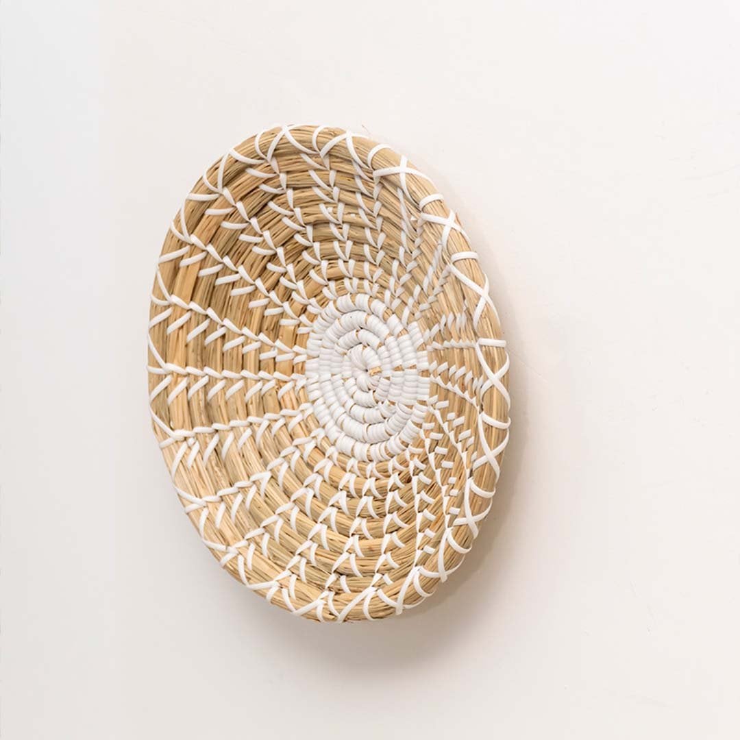 Side view of handwoven round wall decor plate in natural beige with white woven details for interiors.