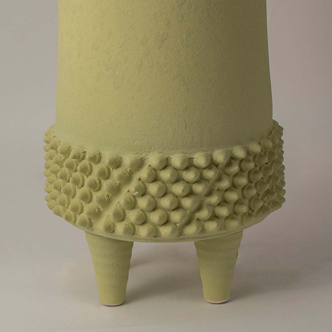 Closeup of green ceramic vase showing detailed textured design on matte finish body with tripod leg handcrafted style.