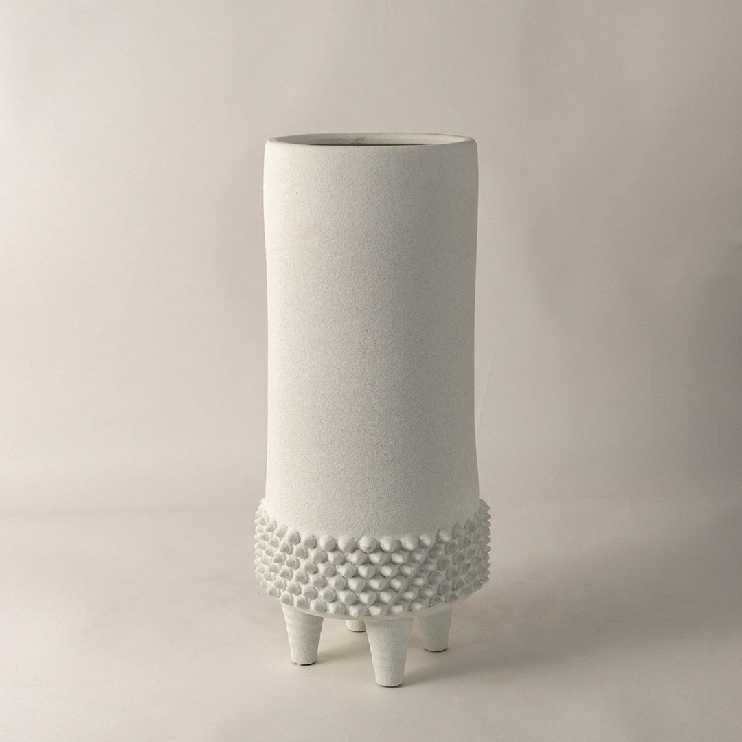 Stylish white ceramic vase with embossed dotted detailing and raised legs placed on white background for modern decor.