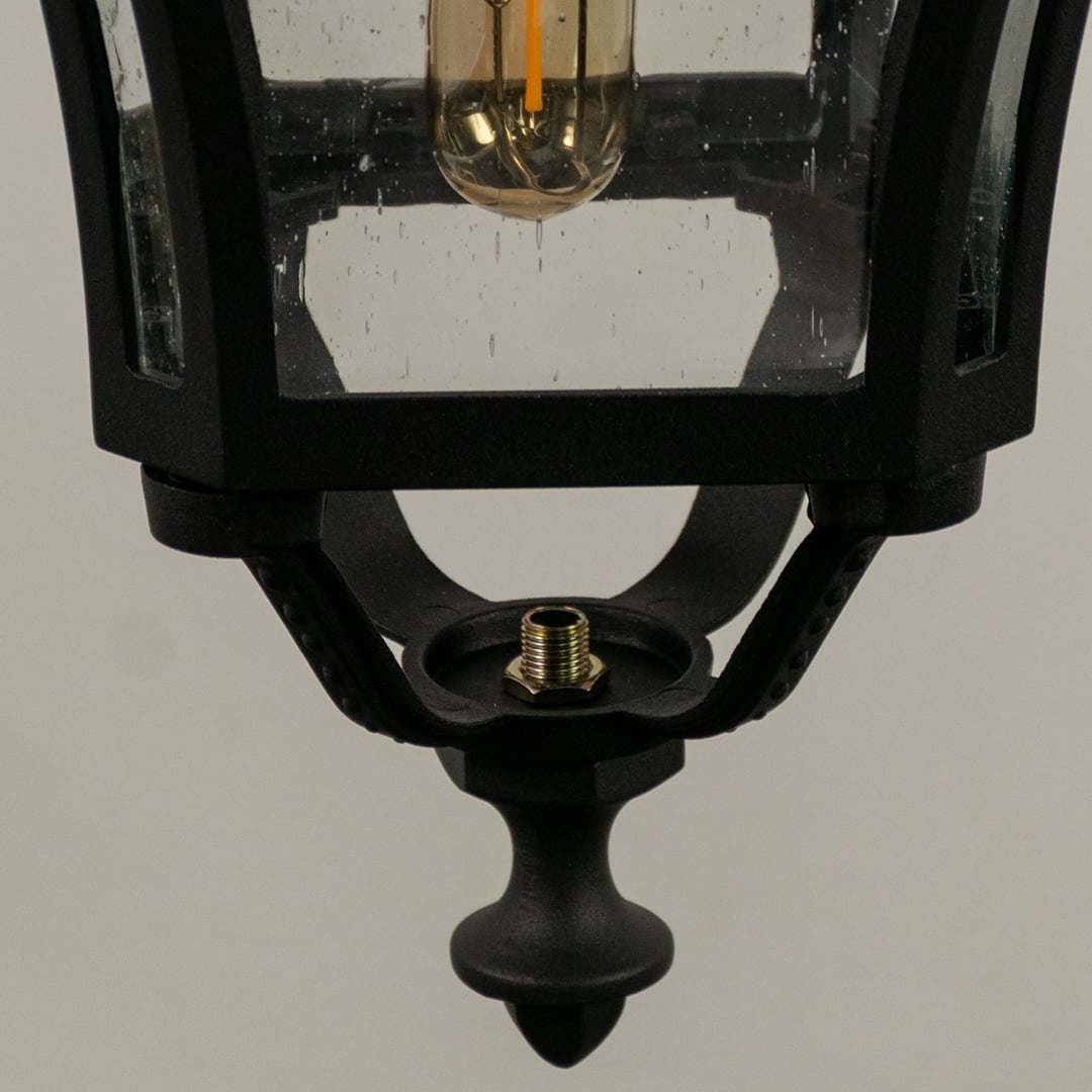 Closeup of black outdoor hanging lantern showing glowing filament bulb textured glass panels and elegant frame design for warm exterior illumination.