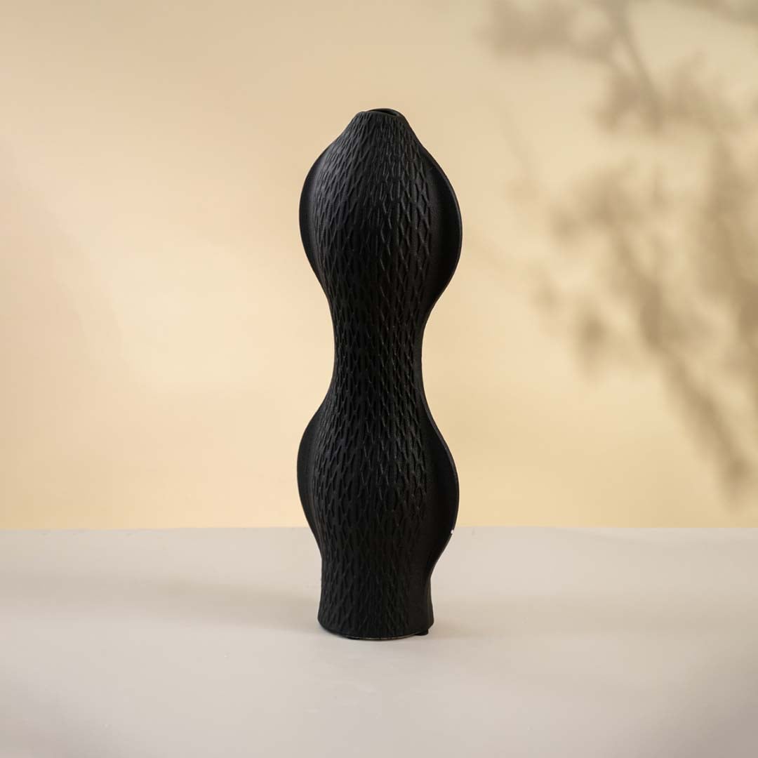 Sculptural black ceramic vase placed on a white surface displaying its modern wave texture and elegant form.