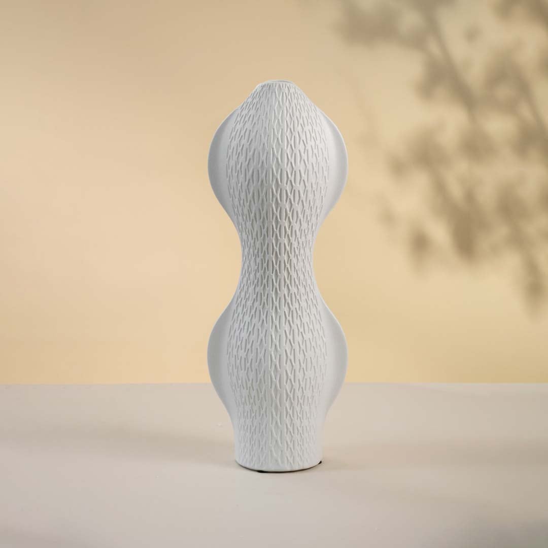 Matte white vase displayed on a white surface emphasizing its curved modern shape and minimal textured pattern.