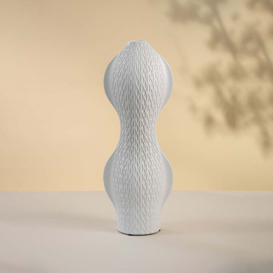 Matte white vase displayed on a white surface emphasizing its curved modern shape and minimal textured pattern.