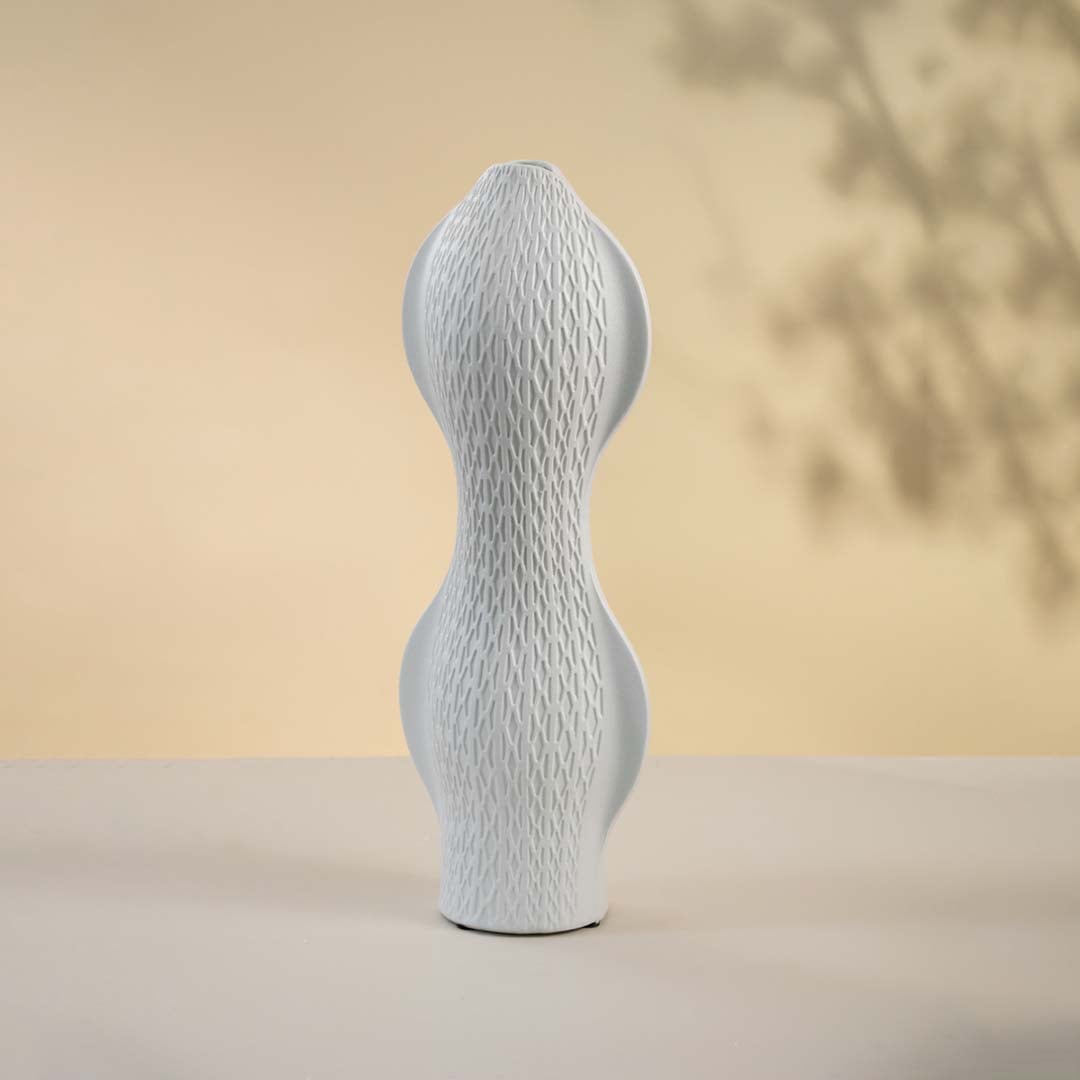 Round white sculptural vase softly illuminated against a white background highlighting fine geometric detailing and artistic form.