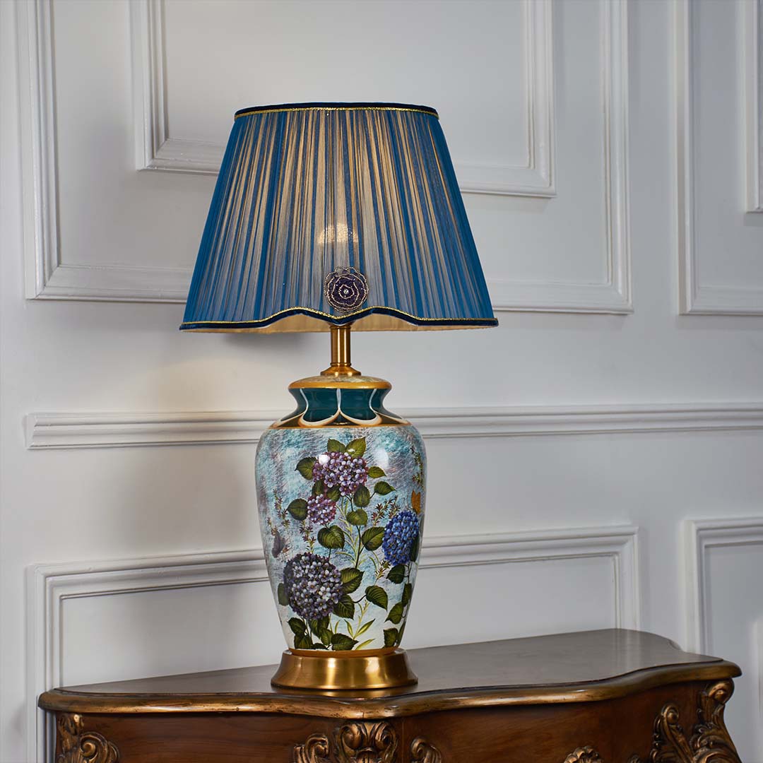 Artistic blue floral ceramic table lamp with gold accents and deep blue pleated shade shown on a white background for premium decor presentation.