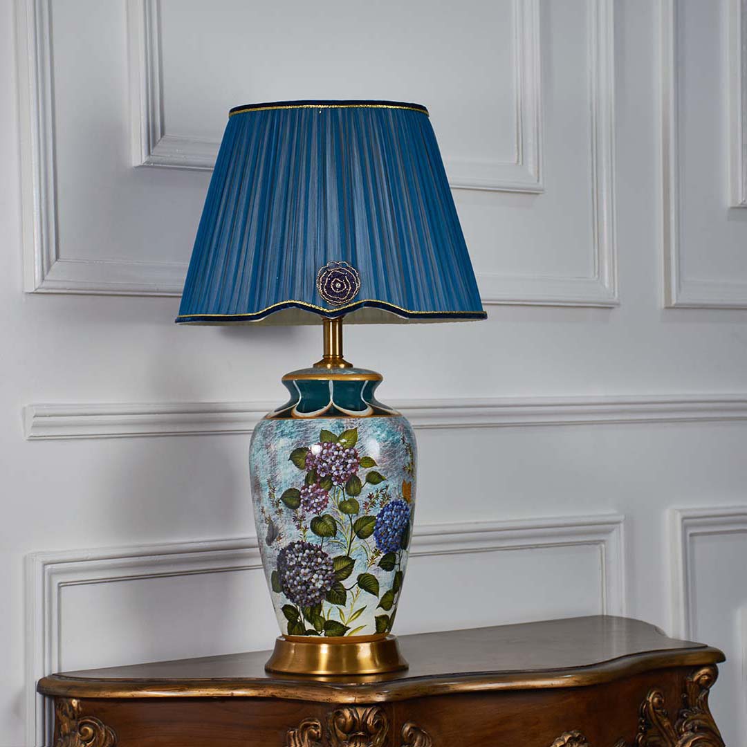 Blue ceramic floral table lamp with gold detailing and pleated blue shade displayed on a clean white background turned off ideal for elegant home decor styling.