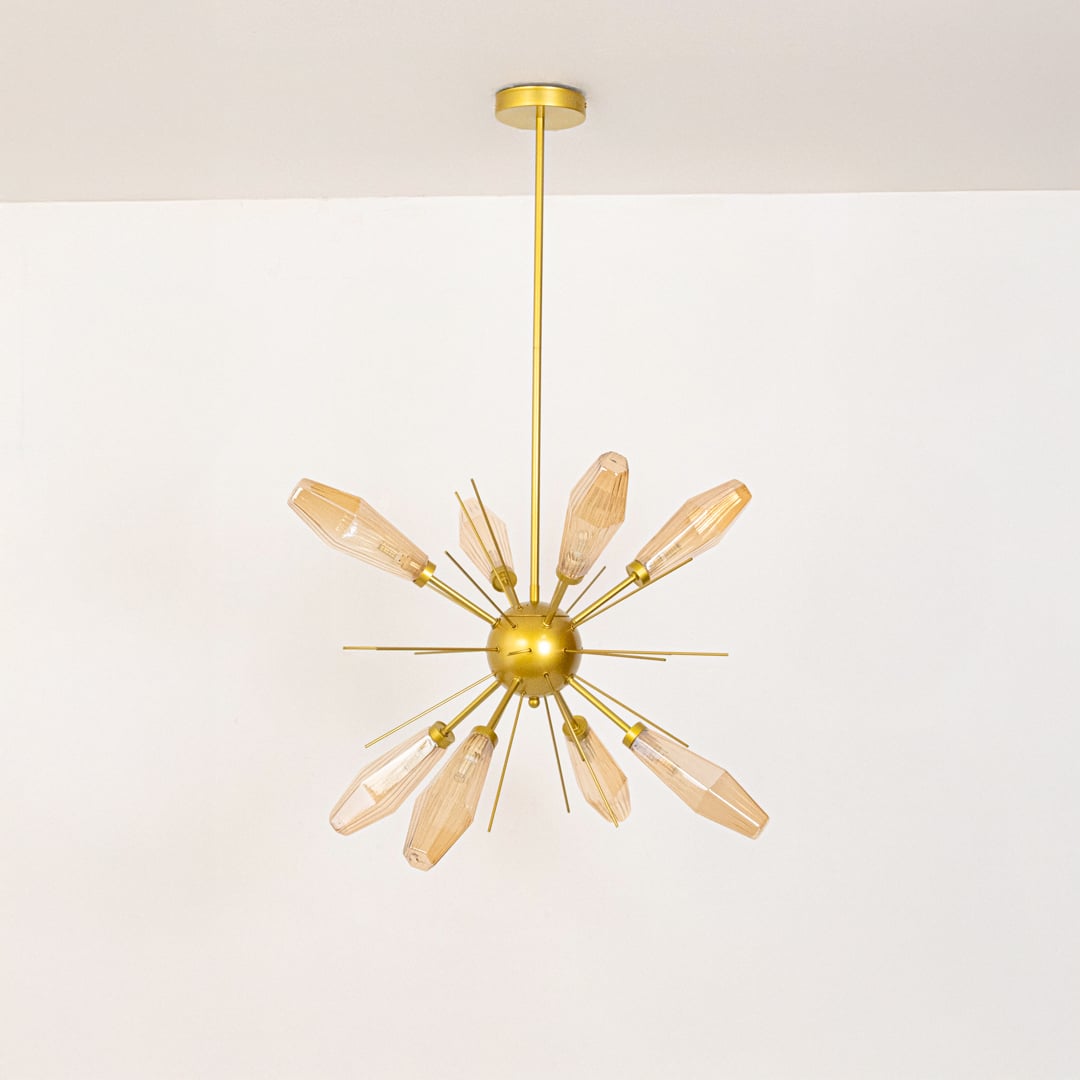 Golden metal chandelier with amber glass rods displayed off on white background highlighting elegant designer ceiling lighting piece.