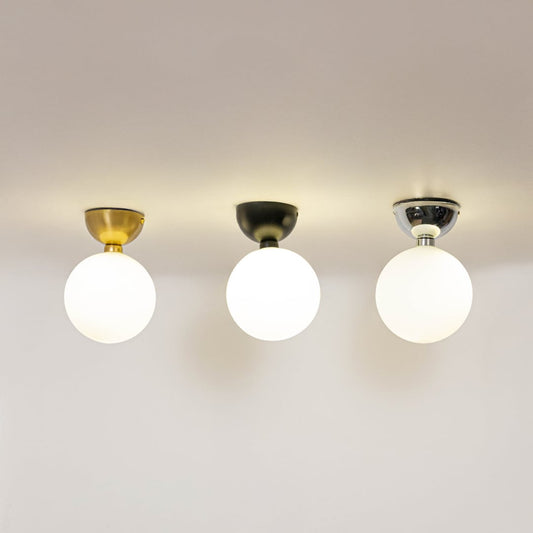 Set of ceiling lights in black gold and chrome finish with frosted glass globes glowing on plain white background.