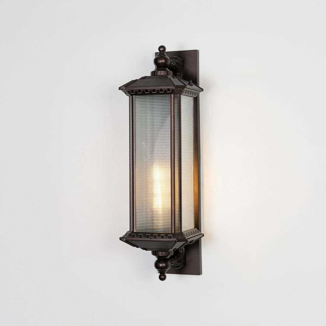 Bronze wall lantern light glowing warmly through frosted glass ideal for outdoor patio or porch lighting decor.