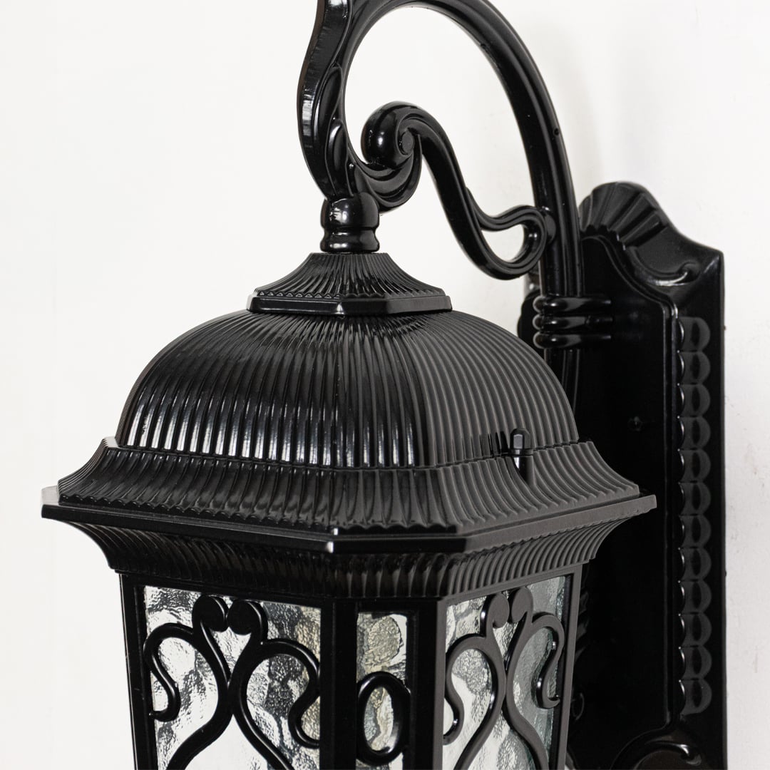 Black metal outdoor wall lantern closeup highlighting ribbed roof scroll arm and clear glass panels for classic exterior lighting decor.