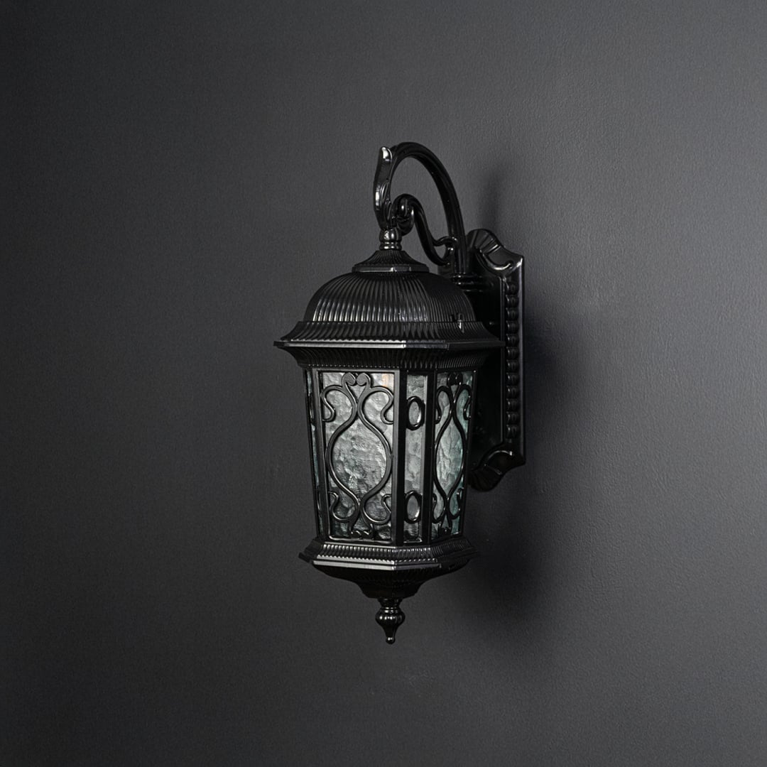 Light off black background presents black metal outdoor wall lantern unlit focusing on curved arm detailing and classic form.