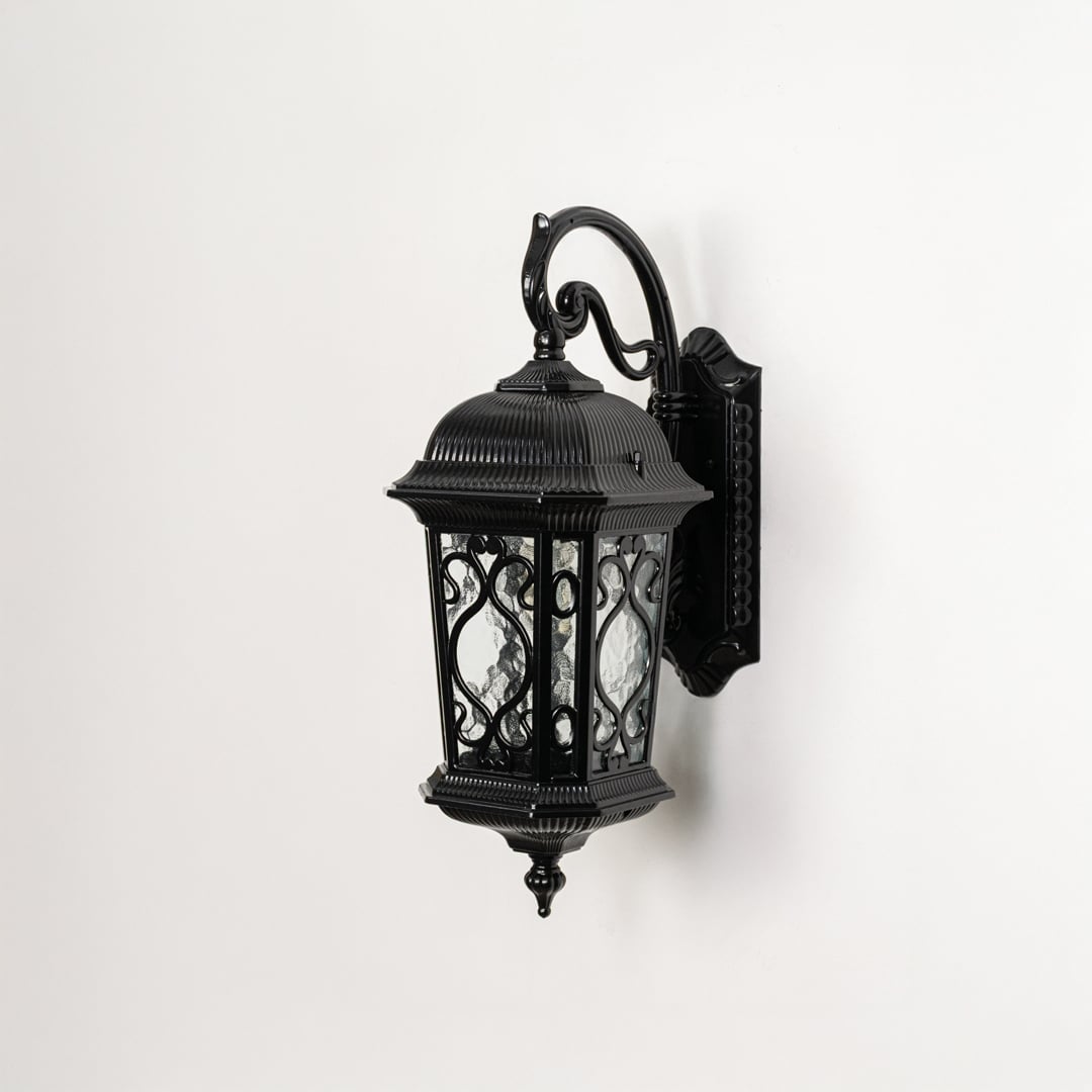 Light off white background displays black metal outdoor wall lantern showcasing ornate design glass texture and sturdy build.