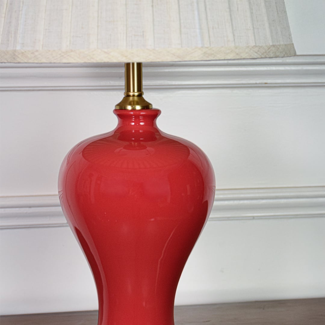 Closeup of red ceramic table lamp highlighting glossy glazed surface elegant curved silhouette and gold metal base.