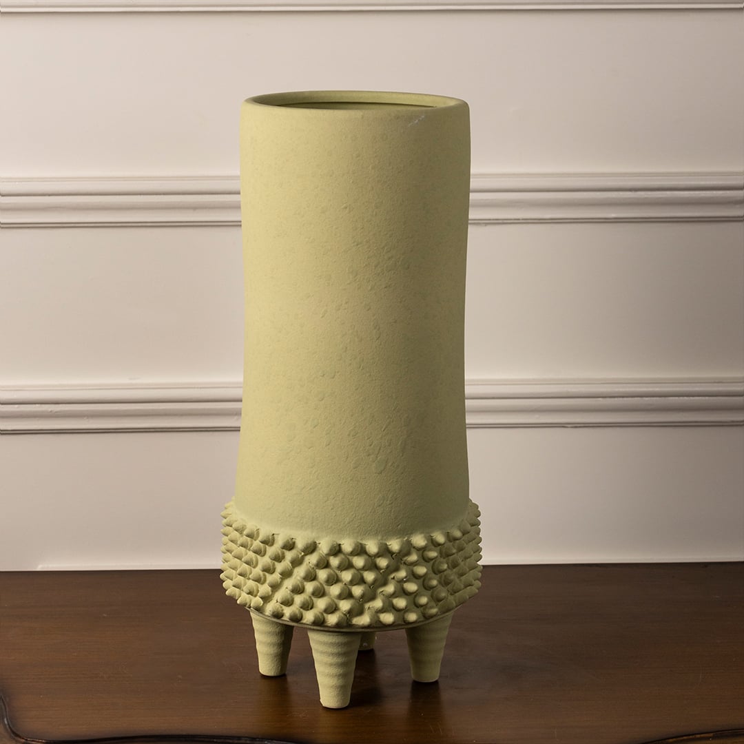 Elegant light green textured ceramic vase with matte finish and tripod stand on white background for decor styling.