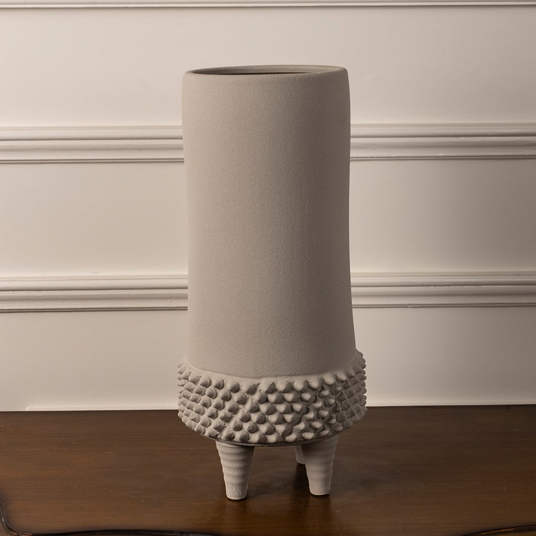 Elegant beige ceramic vase with textured detailing and raised legs shown on plain white background for interior decor.