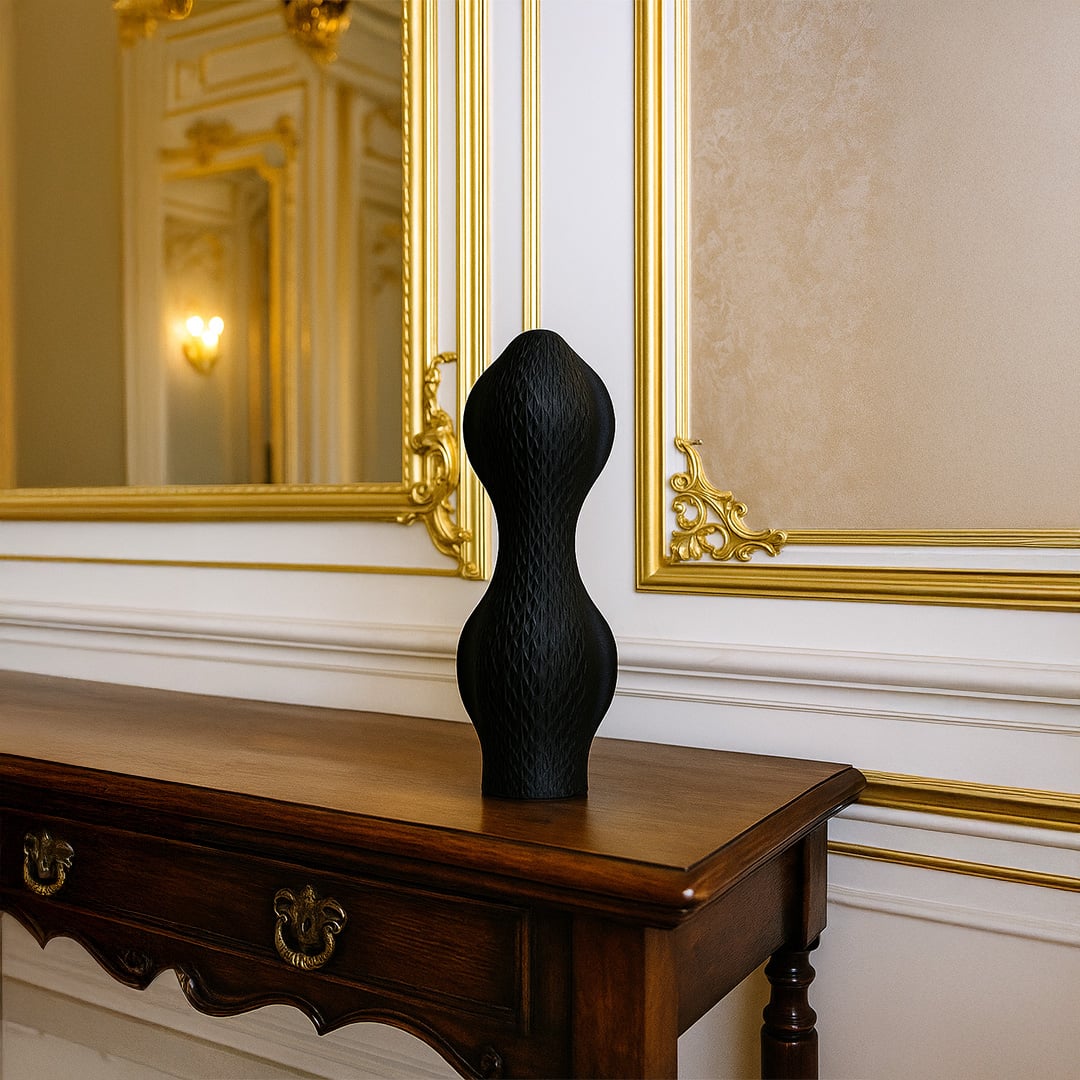 Tall black sculptural vase with a wavy textured surface displayed on a wooden console table in a classic interior featuring gold-trimmed mirrors and elegant lighting.