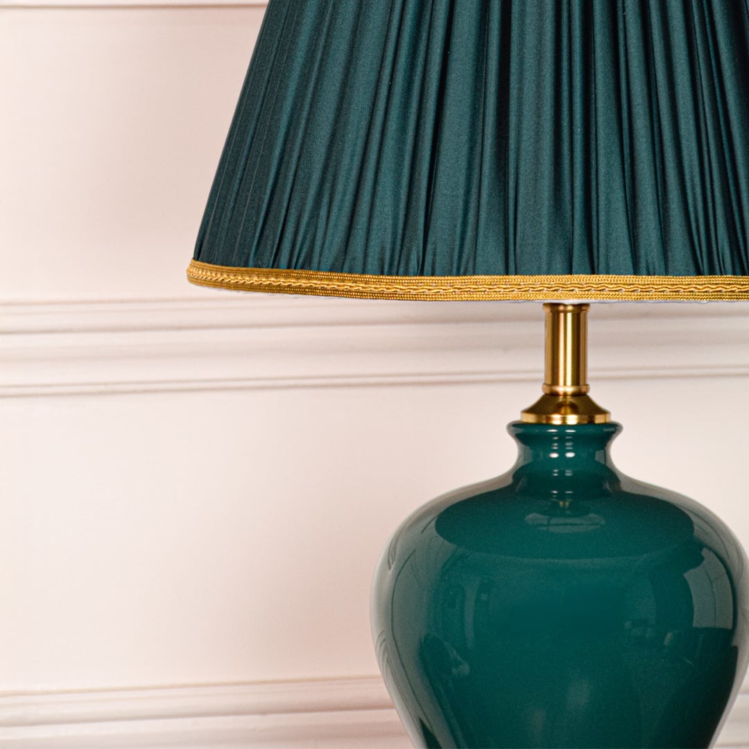 Closeup of teal ceramic table lamp showing glossy glazed surface elegant curved form gold metal base and pleated shade.