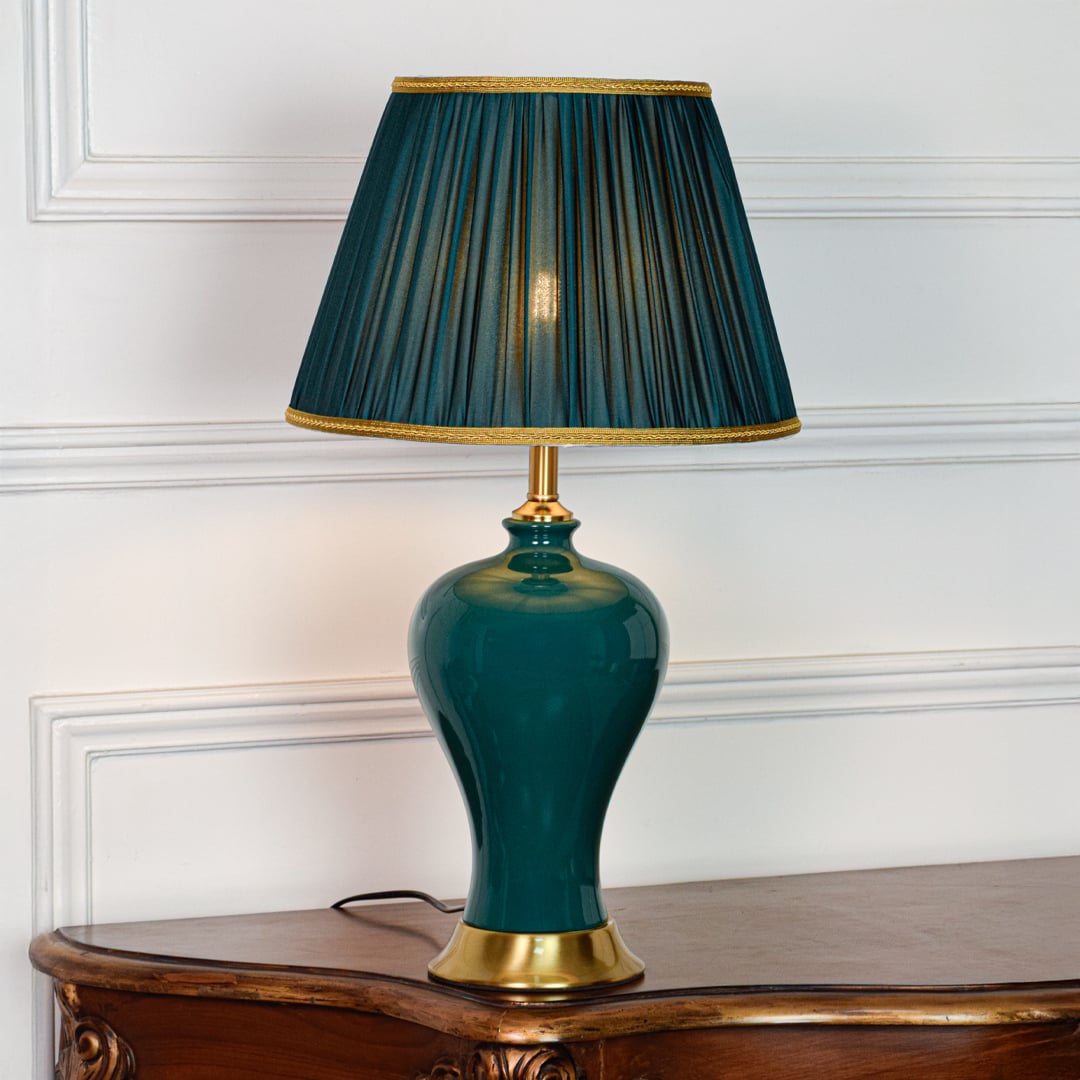 Teal ceramic table lamp featuring smooth glazed finish gold metal base and pleated fabric shade displayed on white background.